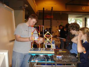 Student handles building model on top of small shake table as other students look on