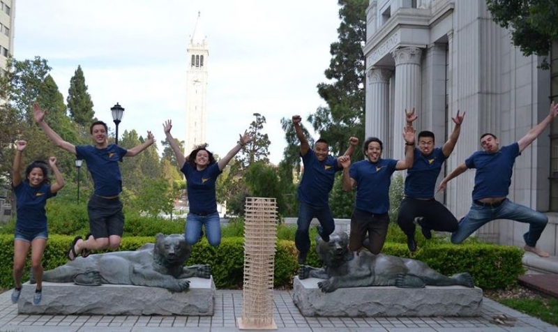 Seismic student team jumping in front of bear statue on Berkeley campus with wooden building model in front of them