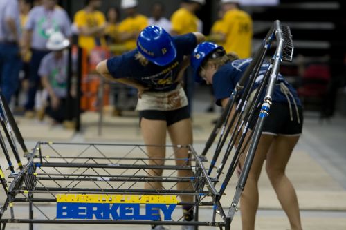 Two female students in hardhats assemble steel bridge